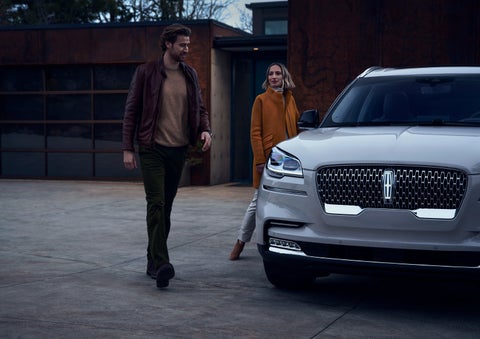 A man and a woman approaching a 2024 Lincoln Aviator® SUV, which illuminates certain lights when they are close | West Point Lincoln in Houston TX